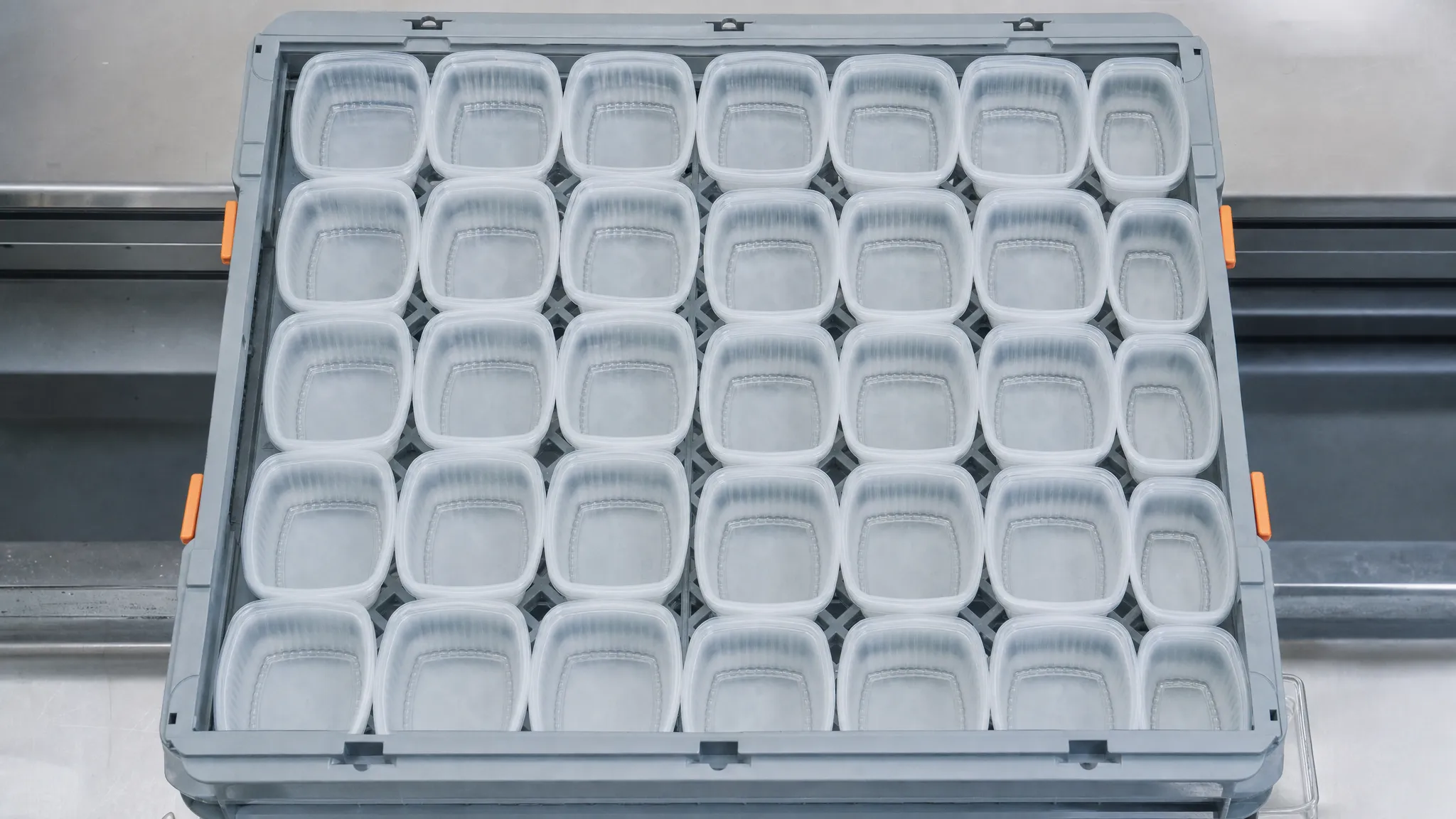 An overhead view of a shallow grey tray holding a tight grid of identical moulded food containers being counted in rows