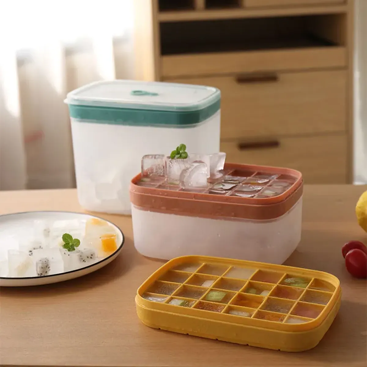 Two plain unmarked storage bins sharing one white body with different coloured lids, teal and terracotta, beside a yellow ice cube tray