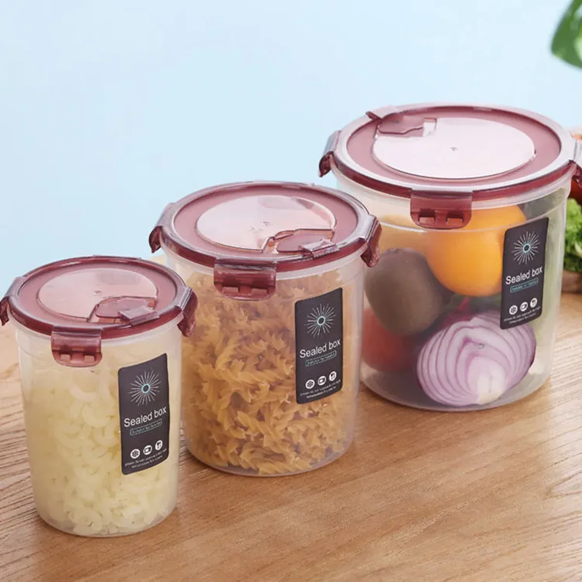 Round PP storage containers with burgundy snap-lock lids holding pasta, onions and fruit on a kitchen counter